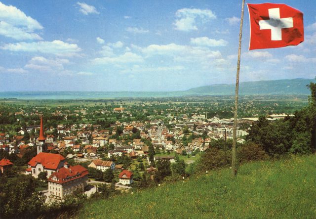 Weiträumiges Panorama mit Schweizerfahne, katholischer Kirche und Bodenseeblick